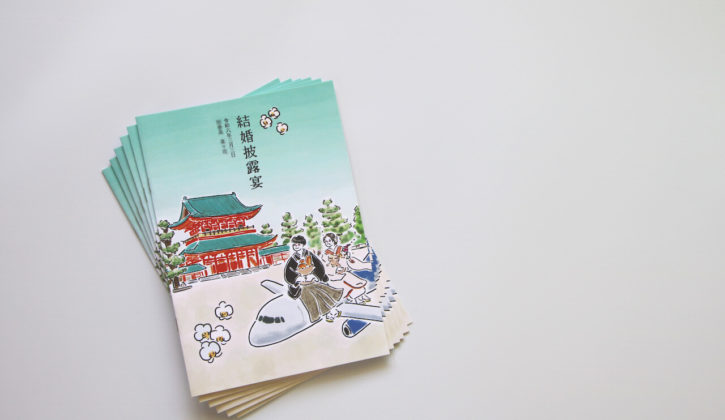 平安神宮外観と飛行機の上に乗っている新郎新婦のイラストが描かれた冊子の表紙